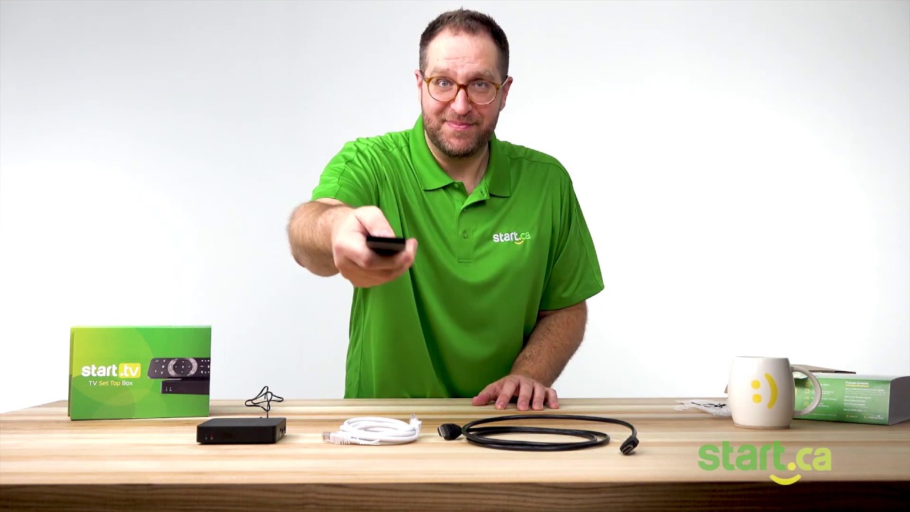 man looking at camera in green shirt gesturing with remote explaining tv set up