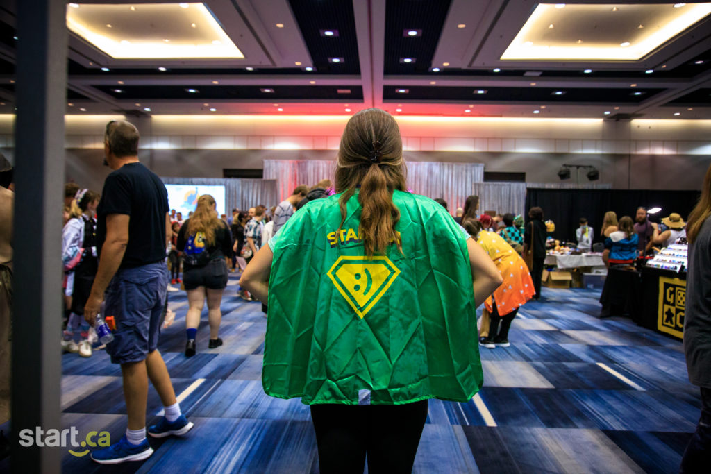Behind an employee showing off their green cape while attending Comiccon