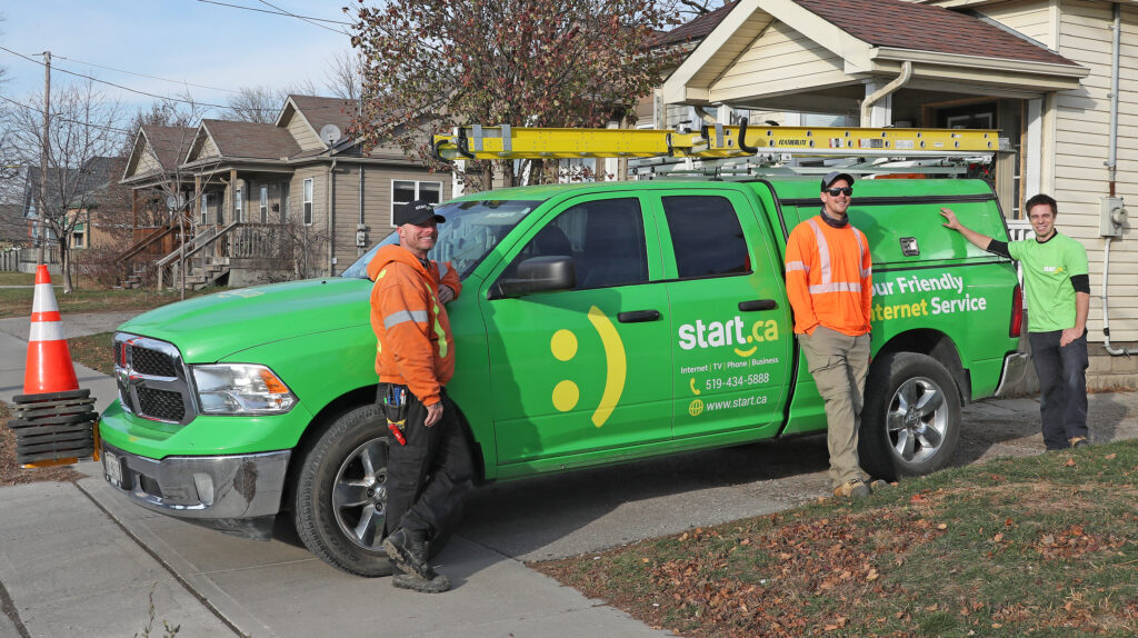 three fibre internet technicians leaning on a green van smiling at the camera. 